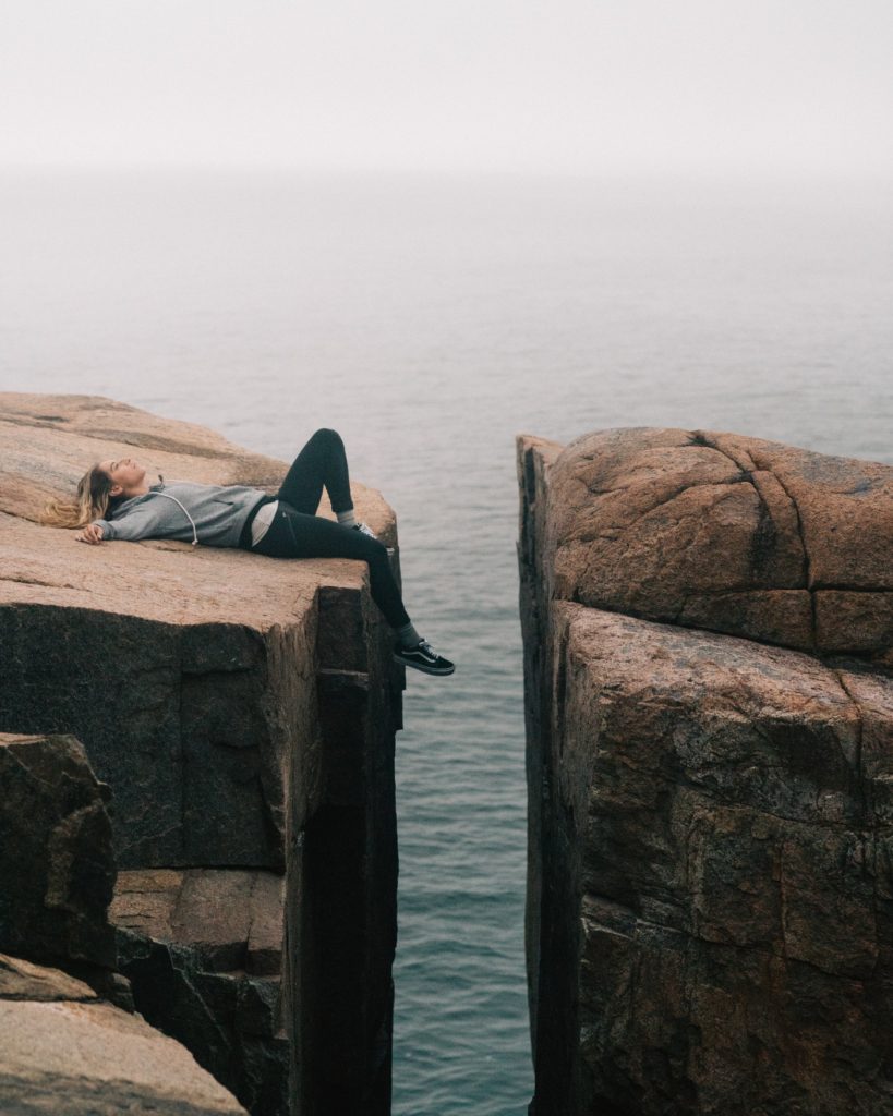 woman lying down on cliff by ocean