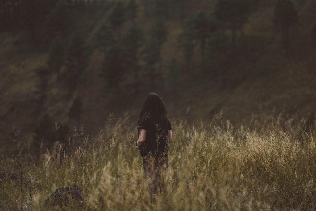 A woman in dark clothing facing away from the camera among a field of wheat and grass